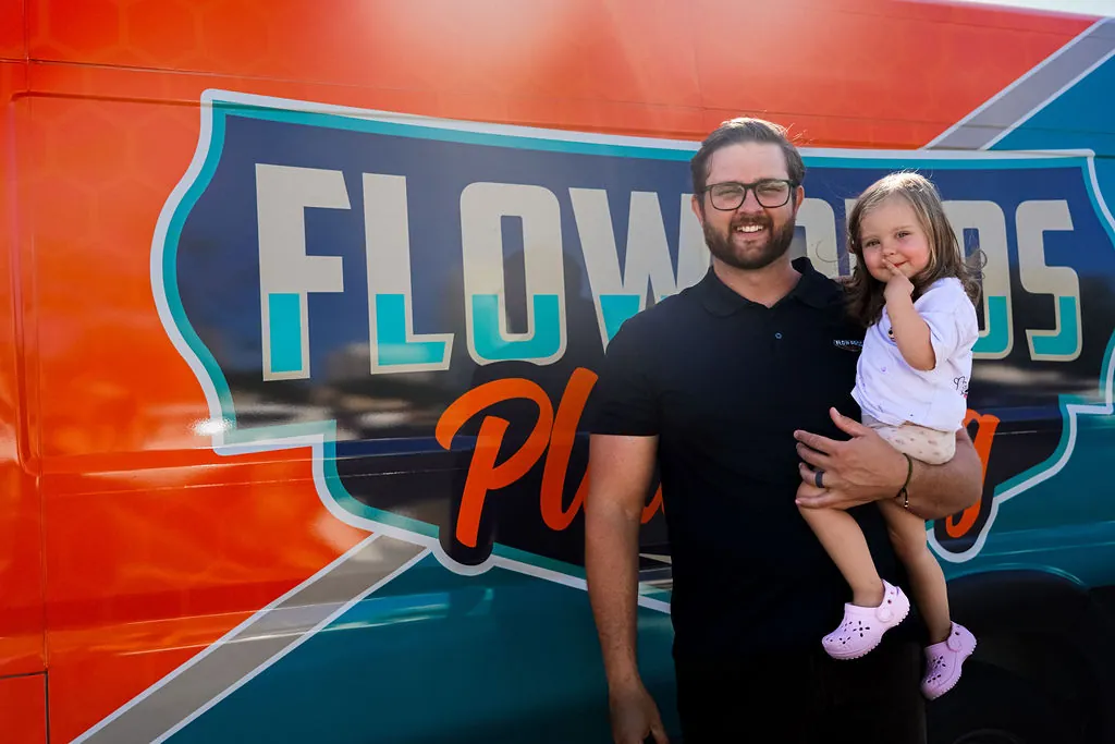 Flow Pros owner Jared holding his young daughter in front of the Flow Pros Plumbing logo on the van