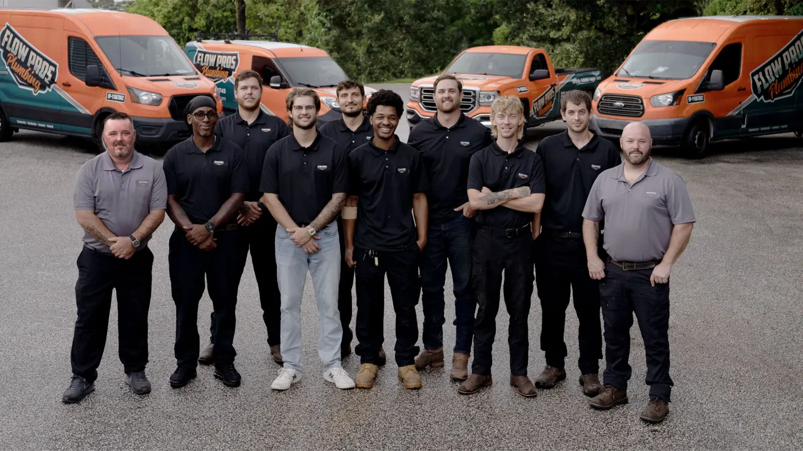 The Flow Pros Plumbing team standing in front of their orange and teal service vans