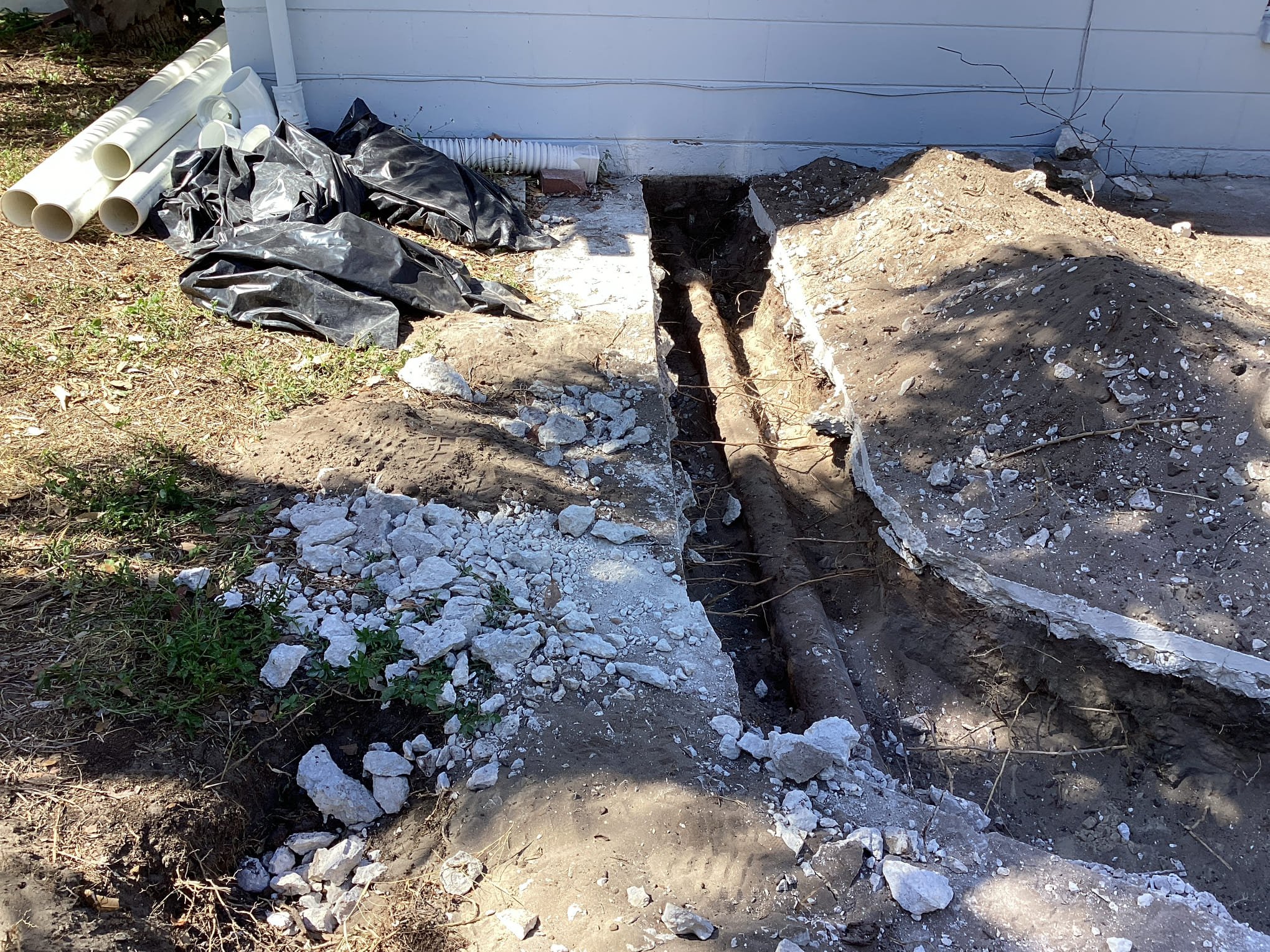 Completed sewer lateral replacement in a Florida front yard showing new PVC pipe in the trench and old corroded cast iron pipe sections laid on the grass